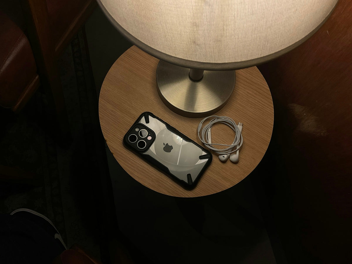 Bedside table with iphone, earbuds, and a lit lamp